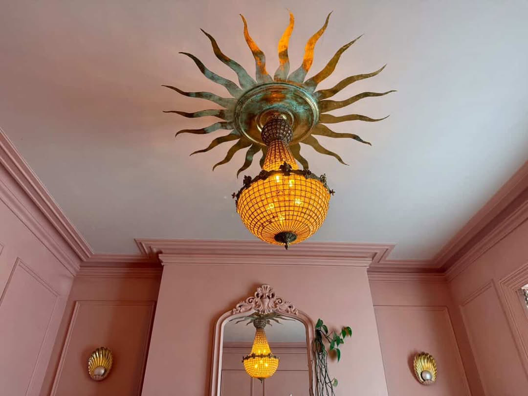 Designed by Lara Bezzina, beautiful antique style chandelier, sitting in the middle of a medallion. Medallion is gilded in gold and a shape of a sun created around the medallion in gold to represent sun. Room paining is light hue of dusty pink.